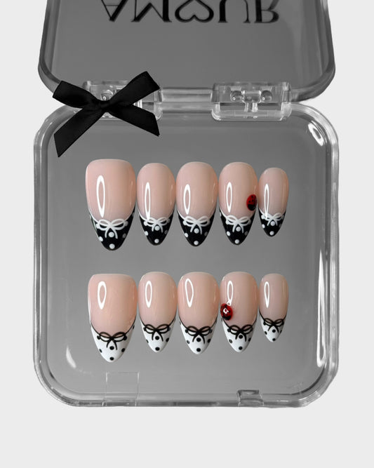 Set of decorative false nails in a clear case with a black bow on a light gray background