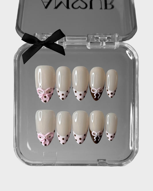 Set of decorative nail art with bows and polka dots in a clear case with a black bow on a white background.