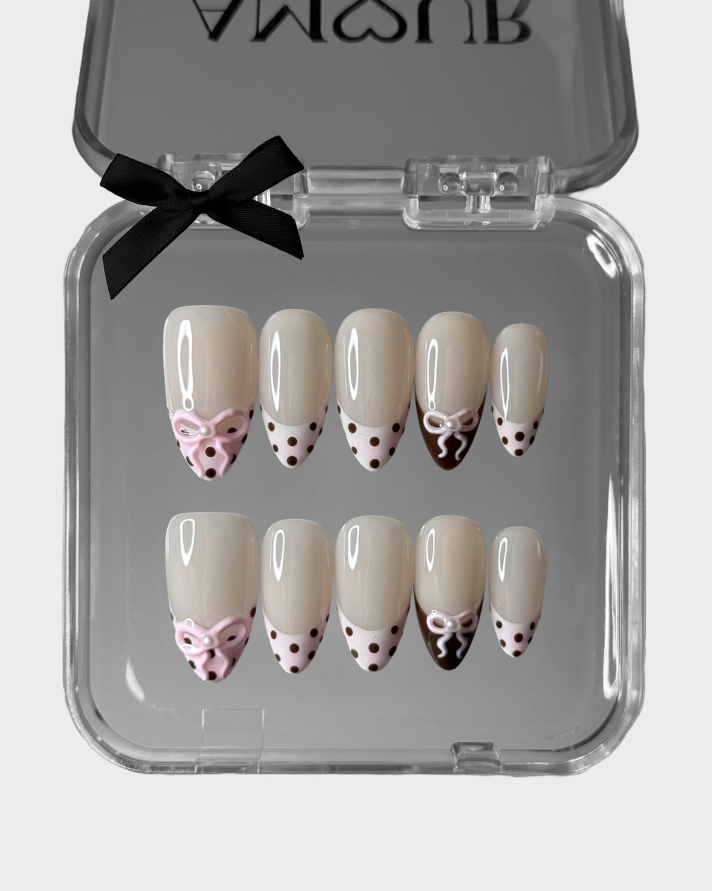 Set of decorative nail art with bows and polka dots in a clear case with a black bow on a white background.