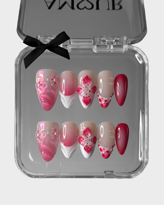 Set of pink and red floral nail designs in a clear case with a black bow.